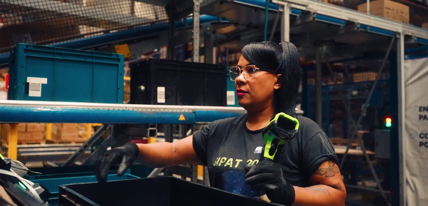 Operadora sorrindo na linha de separação do centro de distribuição